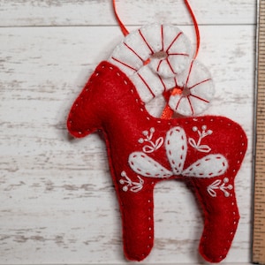 May include: Red felt Christmas ornament shaped like a reindeer with white felt antlers and decorative stitching.