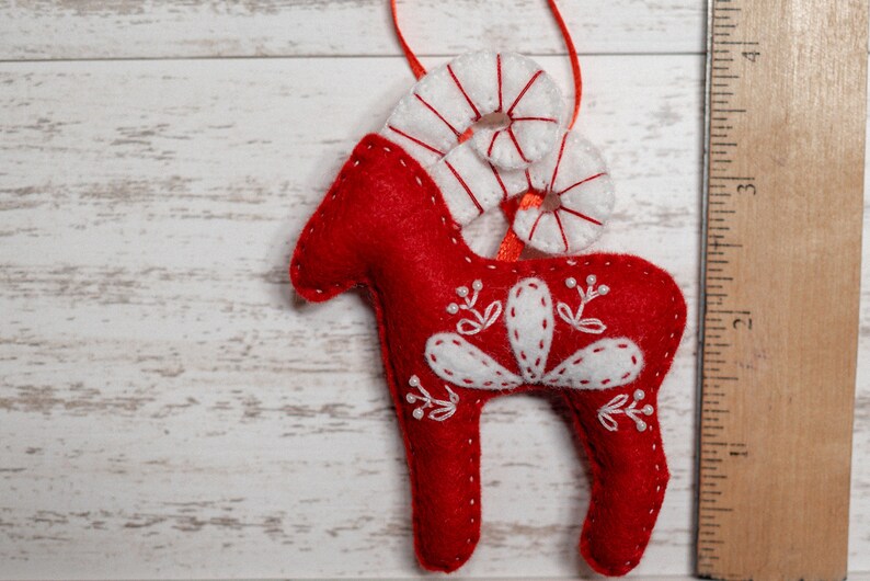 May include: Red felt Christmas ornament shaped like a reindeer with white felt antlers and decorative stitching.