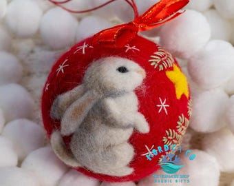 Può includere: Ornamento natalizio rosso con un coniglio bianco, una stella gialla e dettagli a fiocco di neve. L'ornamento ha un nastro rosso per appenderlo. L'ornamento è di The Ornament Shop Nordic Gifts.