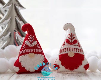 May include: Two felt gnome ornaments with red and white hats and beards. The gnomes are embroidered with white stitching and have a traditional Scandinavian design.