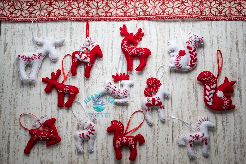 May include: Twelve felt Christmas ornaments in red and white with Scandinavian folk art designs. The ornaments are shaped like reindeer, horses, and squirrels.