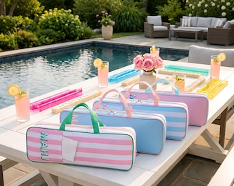 May include: Three rectangular zippered carrying cases for mahjong tiles, arranged in a row on a white outdoor table. The cases feature striped patterns in pink and white, light blue and white, and solid pink, each with top handles and the word MAHJ.