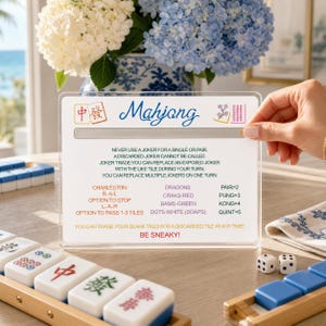 May include: A clear acrylic Mahjong reference card featuring blue script text, red and green Chinese characters, and instructional rules for gameplay. The card lists specific tile combinations and strategies, including the phrase BE SNEAKY! in red.