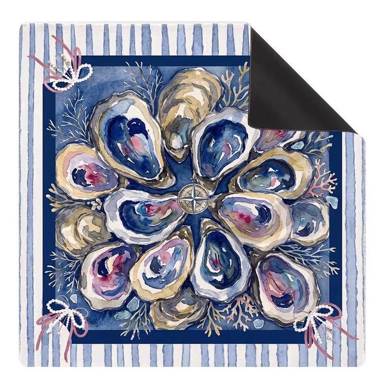 May include: A square mat featuring a watercolor illustration of oyster shells arranged in a circular pattern around a central compass rose. The design includes coral accents, white pearl strands with pink ribbons, and a blue and white striped border.