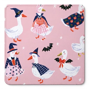 May include: A square mousepad with a light pink background featuring a repeating pattern of white geese dressed in various Halloween costumes, including witch hats, capes, and pumpkin-print outfits, interspersed with small black bats and white stars.