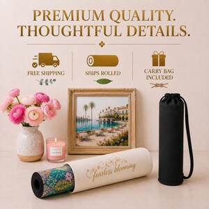 May include: A yoga mat with a colourful floral pattern, partially inside a cream-coloured sleeve featuring the text 'fearless blooming'. Beside it is a black cylindrical carry bag, a framed coastal landscape print, a pink candle, and a vase of pink flowers.