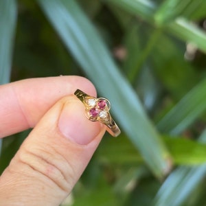 May include: A gold ring with three red gemstones and a single white gemstone set in a clover design.