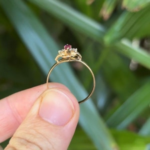 May include: A gold ring with a red gemstone surrounded by smaller clear gemstones.