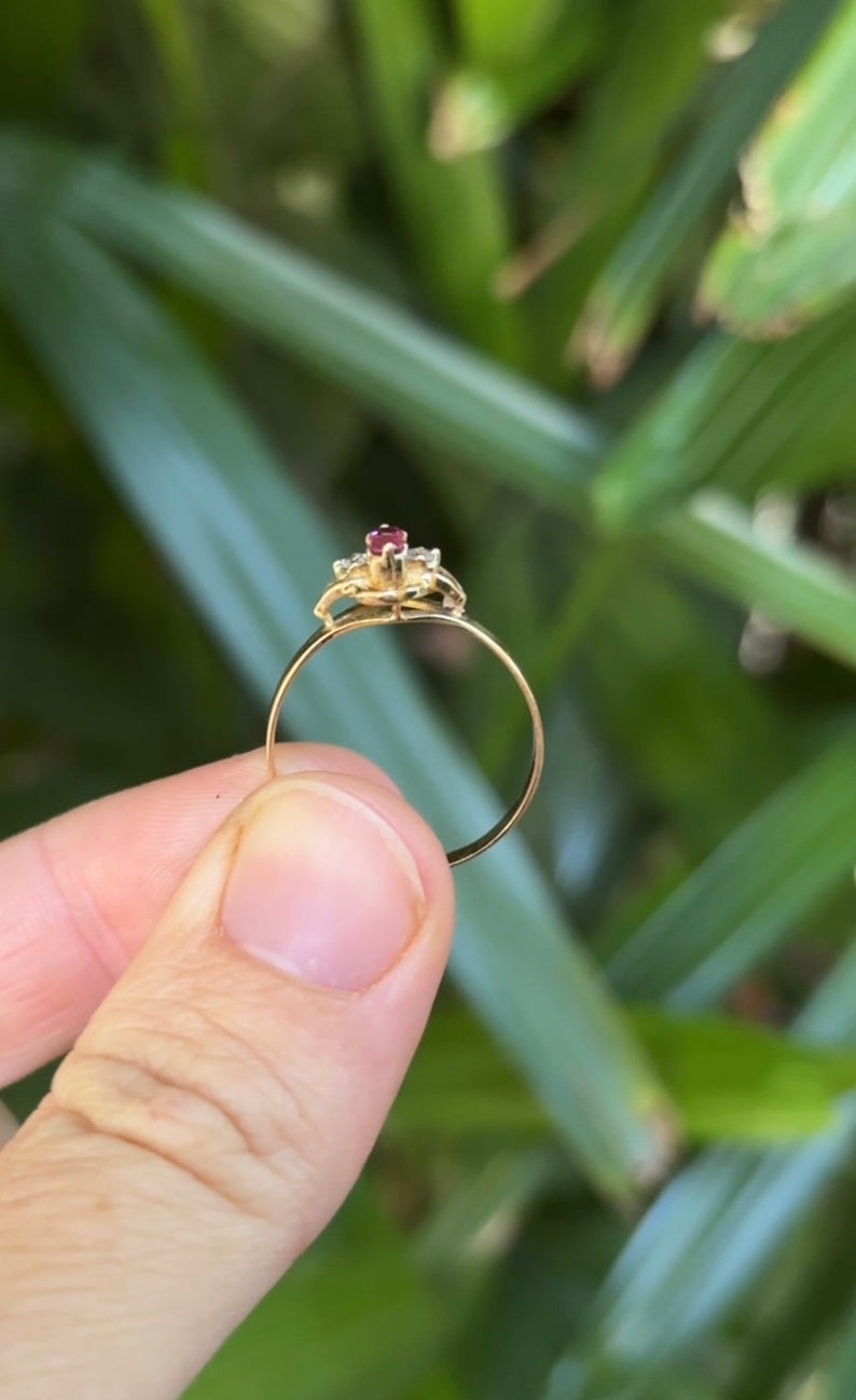 May include: A gold ring with a red gemstone surrounded by smaller clear gemstones.