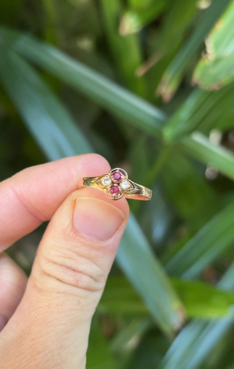 May include: A gold ring with a four-leaf clover design. The ring has three red gemstones and one white gemstone.