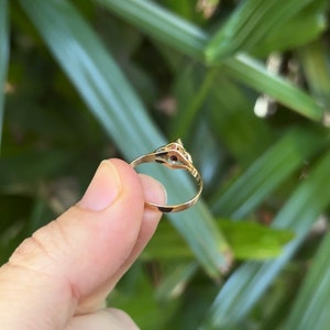 May include: A gold ring with a small red stone set in the center. The ring is simple and elegant.
