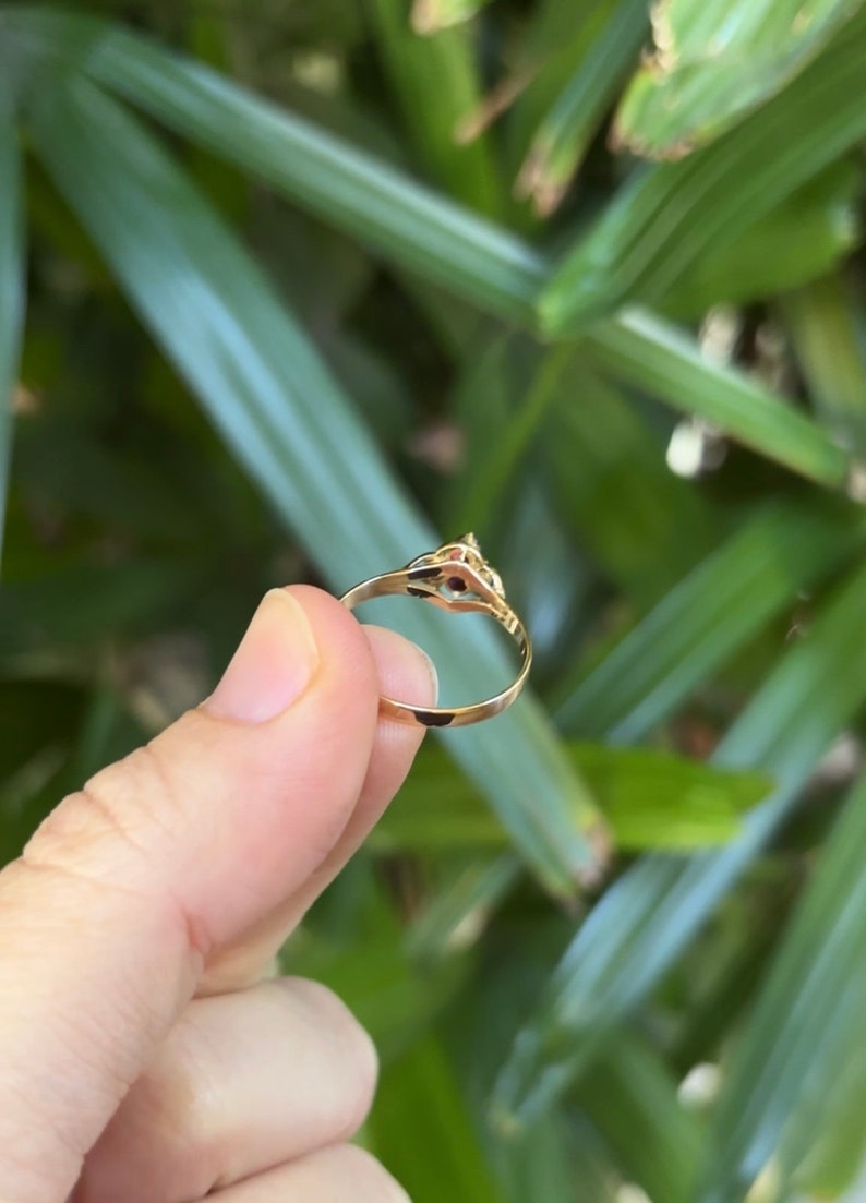 May include: A gold ring with a small red stone set in the center. The ring is simple and elegant.