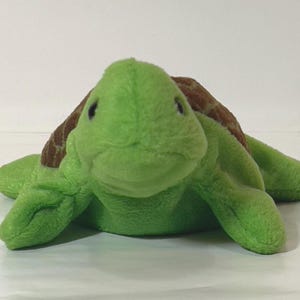 May include: A plush green turtle toy with a brown patterned shell. The turtle has a smiling face and four flipper-like limbs. The toy is designed to resemble a sea turtle.