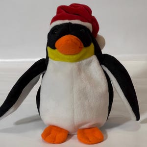 May include: A plush penguin toy with a red and white Santa hat. The penguin has a black head and wings, a white belly, yellow accents, and orange feet and beak. The toy is designed to look like a penguin.