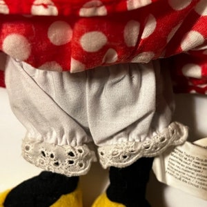 May include: A red and white polka dot dress with white lace trim and black shoes. The dress has a white petticoat underneath. The doll is wearing a red and white polka dot dress with white lace trim and black shoes. The dress has a white petticoat underneath.