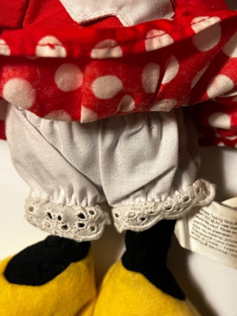 May include: A red and white polka dot dress with white lace trim and black shoes. The dress has a white petticoat underneath. The doll is wearing a red and white polka dot dress with white lace trim and black shoes. The dress has a white petticoat underneath.