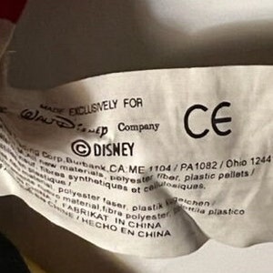 May include: White tag with black text that reads "MADE EXCLUSIVELY FOR Walt Disney Company &copy;DISNEY Corp. Burbank CA: ME 1104/PA1082/Ohio 12441/ New materials, polyester fiber, plastic pellets/ Fibres synth&eacute;tiques et cellulosiques.  Polyester faser, plastik  /  Material fibra polyester  /  FABRIKAT IN CHINA  /  HECHO EN CHINA" and a CE mark.