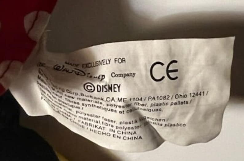 May include: White tag with black text that reads "MADE EXCLUSIVELY FOR Walt Disney Company &copy;DISNEY Corp. Burbank CA: ME 1104/PA1082/Ohio 12441/ New materials, polyester fiber, plastic pellets/ Fibres synth&eacute;tiques et cellulosiques.  Polyester faser, plastik  /  Material fibra polyester  /  FABRIKAT IN CHINA  /  HECHO EN CHINA" and a CE mark.