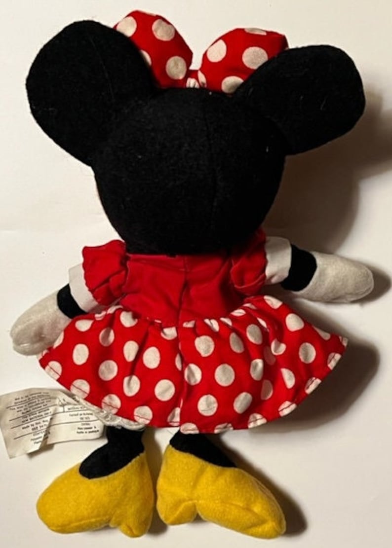 May include: A red and white polka dot dress with a black bow on top of the head. The plush toy is wearing yellow shoes.