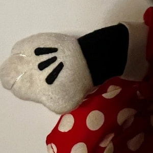May include: A white plush glove with black finger details, attached to a red and white polka dot fabric.