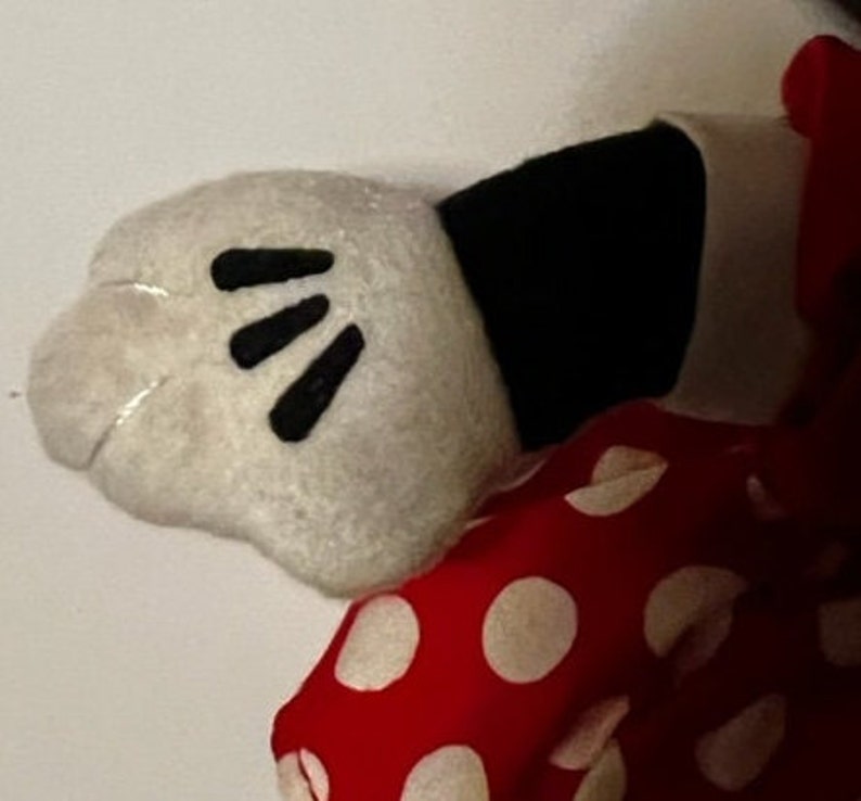 May include: A white plush glove with black finger details, attached to a red and white polka dot fabric.