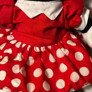 May include: A red plush toy with white polka dots, a white collar, and a red bow. The toy is dressed in a red dress with white polka dots.