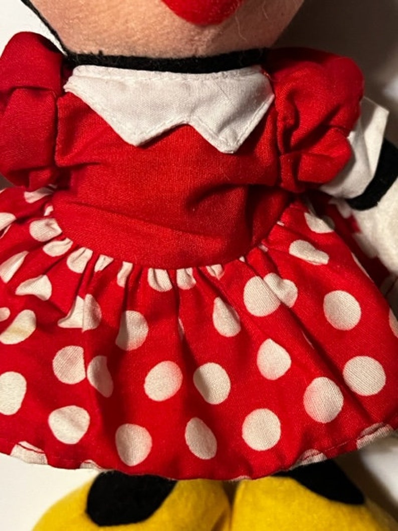 May include: A red plush toy with white polka dots, a white collar, and a red bow. The toy is dressed in a red dress with white polka dots.