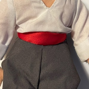 May include: A white shirt with a red sash around the waist and black pants. The shirt has a V-neck and a small opening at the neckline.