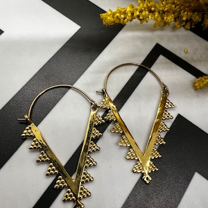 May include: A pair of gold hoop earrings with a V-shaped design. The earrings have a textured, hammered finish and a scalloped edge.