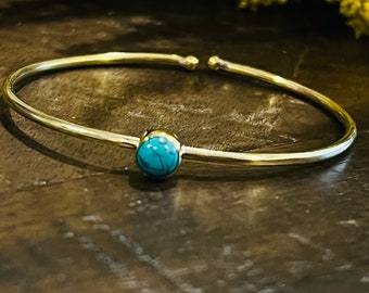 May include: A silver bangle bracelet with a turquoise stone accent.