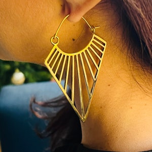 May include: Gold geometric hoop earrings with a triangular shape and a sunburst design.