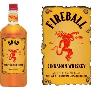 Pu&ograve; includere: Un'etichetta personalizzata per una bottiglia di whisky alla cannella Fireball con un design rosso, caldo e infuocato. L'etichetta presenta un demone rosso con fiamme e il testo "FIREBALL" in uno schema di colori giallo, arancione e rosso. L'etichetta include anche il testo "BRAD" e "BUON 21&deg; COMPLEANNO".