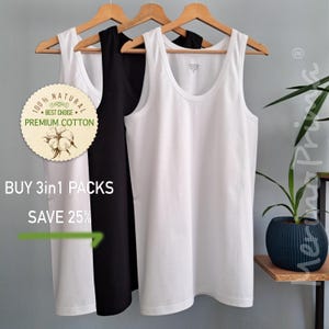 May include: Three sleeveless shirts, one white and two black, hanging on wooden hangers. The white shirt has a label that reads "100% NATURAL BEST CHOICE PREMIUM COTTON". The text "BUY 3in1 PACKS SAVE 25%" is visible below the shirts.