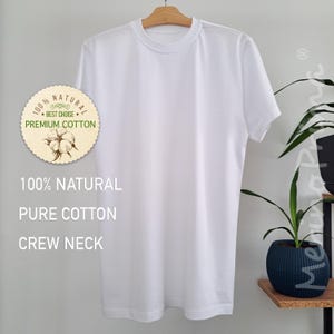 May include: White t-shirt with a crew neck. The shirt has a label that says "100% NATURAL BEST CHOISE PREMIUM COTTON". The text "100% NATURAL PURE COTTON CREW NECK" is printed below the label.