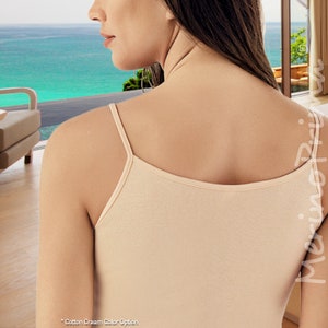 May include: A close-up of a woman wearing a beige tank top. The tank top has thin straps and a scoop neck. The woman is facing away from the camera.