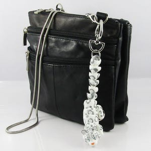 May include: A black leather shoulder bag with a silver chain strap and a white snow leopard charm attached to the zipper pull.