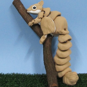 May include: A brown and tan articulated squirrel figurine with a long, curled tail. The squirrel is perched on a brown branch.