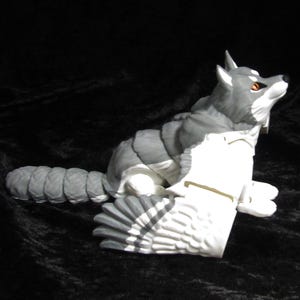 May include: A grey and white wolf figurine with wings. The wolf is sitting with its head tilted up and its eyes open. The wings are spread out behind the wolf.