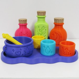 May include: A set of colourful plastic potion-making toys including a purple cauldron with a yellow stirring rod, three bottles with tan caps in pink, green, and orange, and three small cups in yellow, blue, and orange, all on a purple tray.