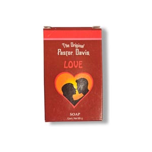 May include: Red and orange soap bar packaging with a silhouette of a couple kissing inside a heart. The packaging reads "The Original Pastor Davis LOVE SOAP Cont. Net 85 g".