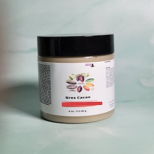 May include: A 4 ounce jar of Gres Cacao body butter. The jar is labeled with the words "Gres Cacao" and "4 oz, 113.40 g". The label also features a colorful illustration of cocoa beans, leaves, and flowers.