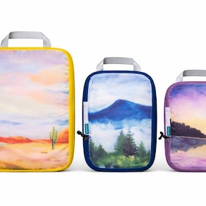 May include: Three travel organisers with landscape art. The largest has a yellow border and a desert scene. The middle one has a blue border and a mountain scene. The smallest has a purple border and a lake scene.