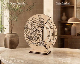 May include: A circular wooden perpetual calendar featuring a laser-engraved bird and berry branch design. The calendar displays the text 'JAN', 'MAR', 'APR', 'MAY', 'JUN', 'MON', 'TUE', 'WED', 'TH', and numbers 1 through 13 on rotating rings.