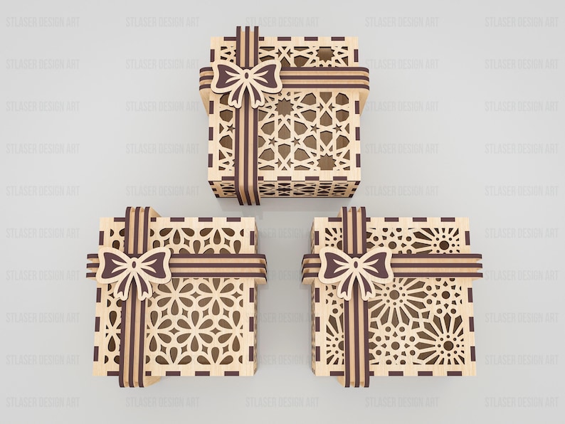 May include: Three square gift boxes made of light-colored wood with dark brown accents. Each box features intricate laser-cut geometric patterns on the lid and sides, topped with a decorative dark brown wooden bow and ribbon detail.