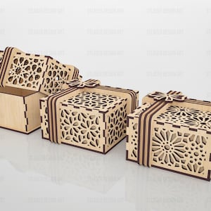 May include: Three square wooden gift boxes with laser-cut geometric patterns on the lids and sides. Each box features a decorative wooden bow on top and dark brown edges. One box is shown open with its lid tilted, while two are closed.