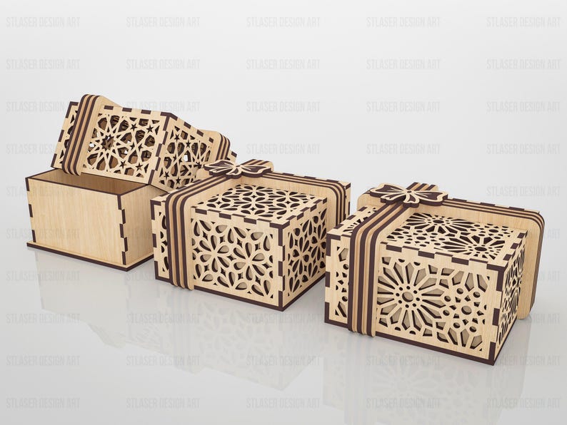 May include: Three square wooden gift boxes with laser-cut geometric patterns on the lids and sides. Each box features a decorative wooden bow on top and dark brown edges. One box is shown open with its lid tilted, while two are closed.