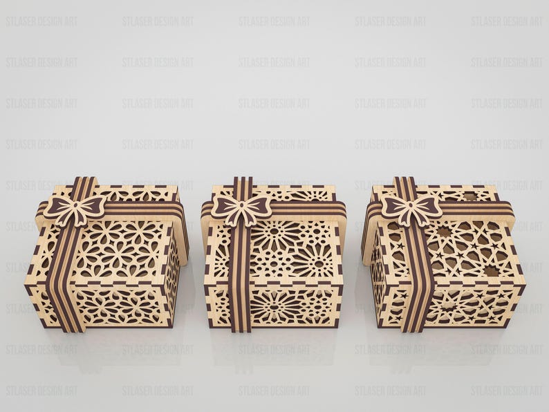 May include: Three square wooden gift boxes featuring intricate laser-cut geometric patterns on the sides and lids. Each box is adorned with a decorative wooden ribbon and bow element in a darker brown tone, contrasting with the light tan wood.