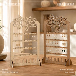 Könnte beinhalten: Zwei helle Holzständer für Ohrringe mit einem lasergeschnittenen Blumenmuster an der Oberseite. Jeder Ständer verfügt über vier horizontale Leisten mit kleinen Löchern zum Aufhängen von Ohrringen und einen Sockel mit Schlitzen. Text umfasst Digital Download, Formats CDR DXF PDF SVG und Material Thickness 3mm 4mm.