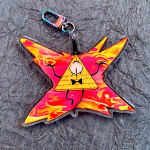May include: A yellow triangle with a single eye and a bow tie, with outstretched arms, is surrounded by a red and orange swirl pattern. The triangle is on a clear acrylic keychain with a silver metal clasp.