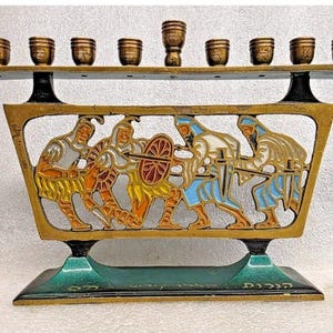 Puede incluir: Una menorá de latón con una base decorativa y una parte superior con nueve candelabros. La base presenta un relieve colorido de figuras en batalla. La menorá es un símbolo judío tradicional.
